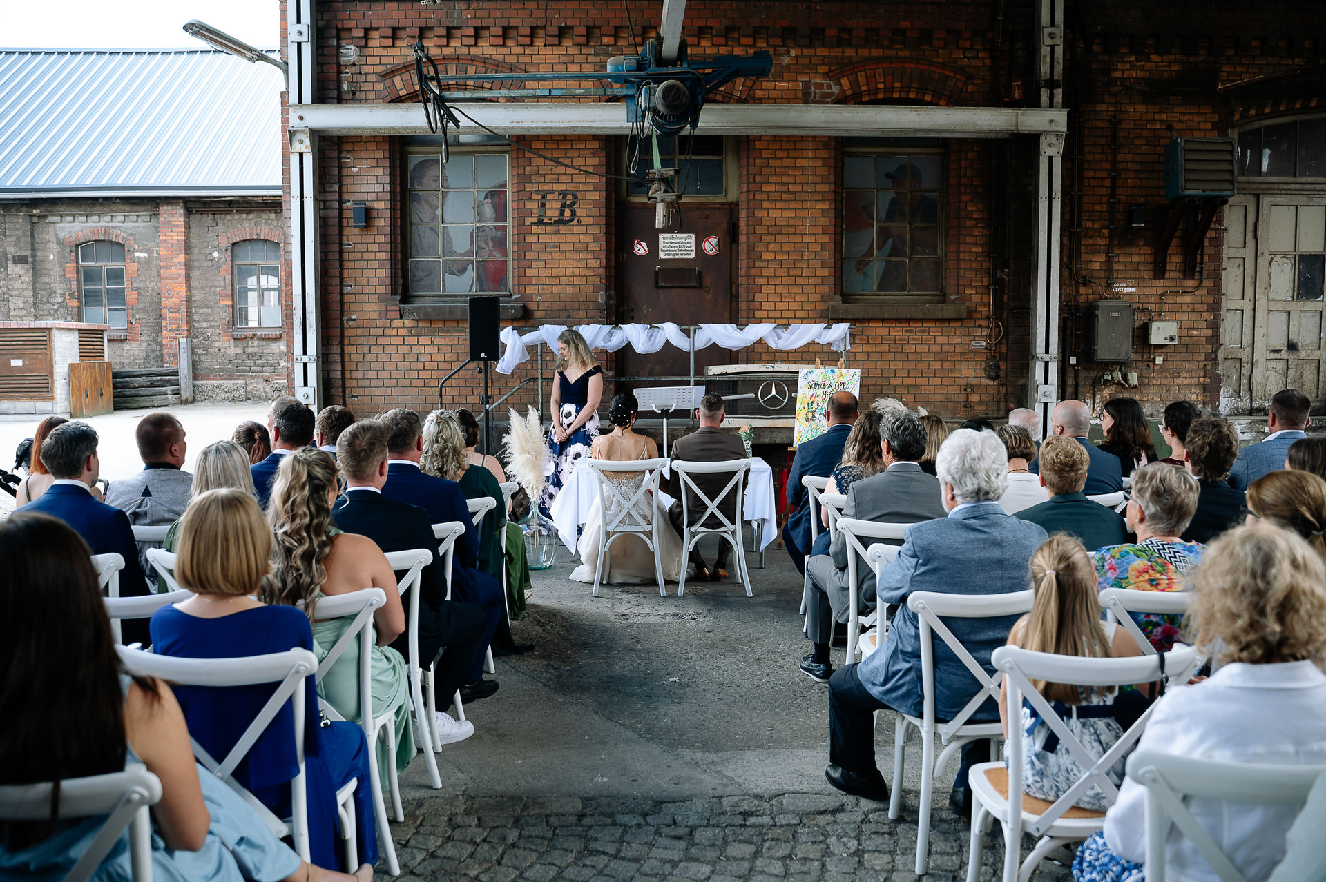 Brautpaar Sara und Olli bei ihrer Hochzeit in der Motorworld Village Metzingen vor historischer Backsteinkulisse.