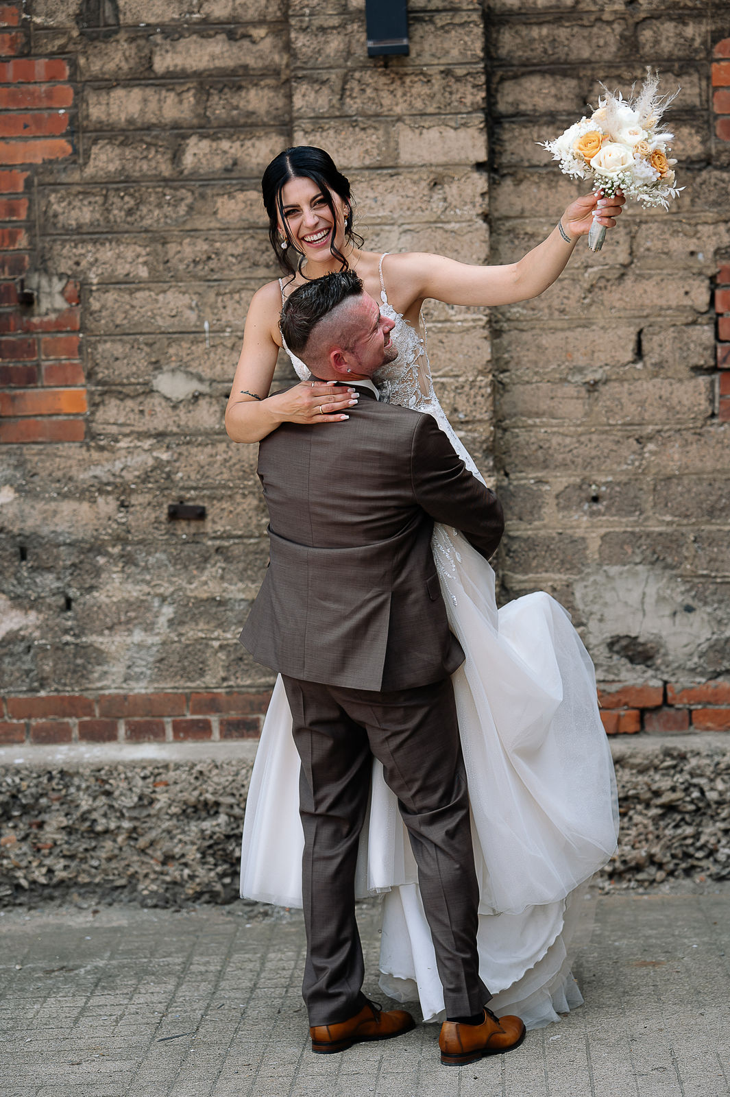 Brautpaar Sara und Olli bei ihrer Hochzeit in der Motorworld Village Metzingen vor historischer Backsteinkulisse.