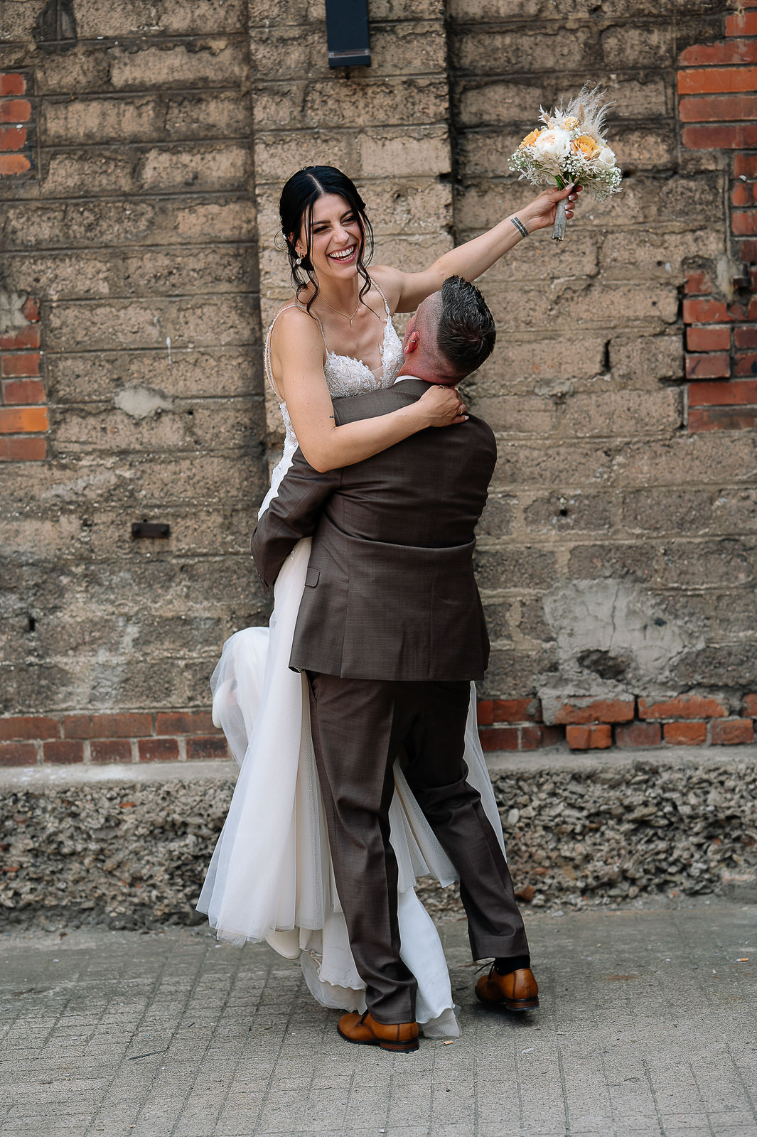 Brautpaar Sara und Olli bei ihrer Hochzeit in der Motorworld Village Metzingen vor historischer Backsteinkulisse.