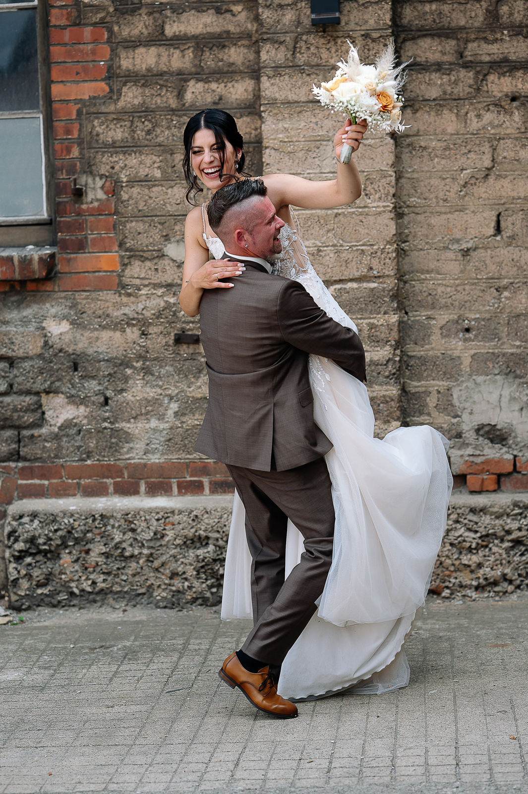 Brautpaar Sara und Olli bei ihrer Hochzeit in der Motorworld Village Metzingen vor historischer Backsteinkulisse.