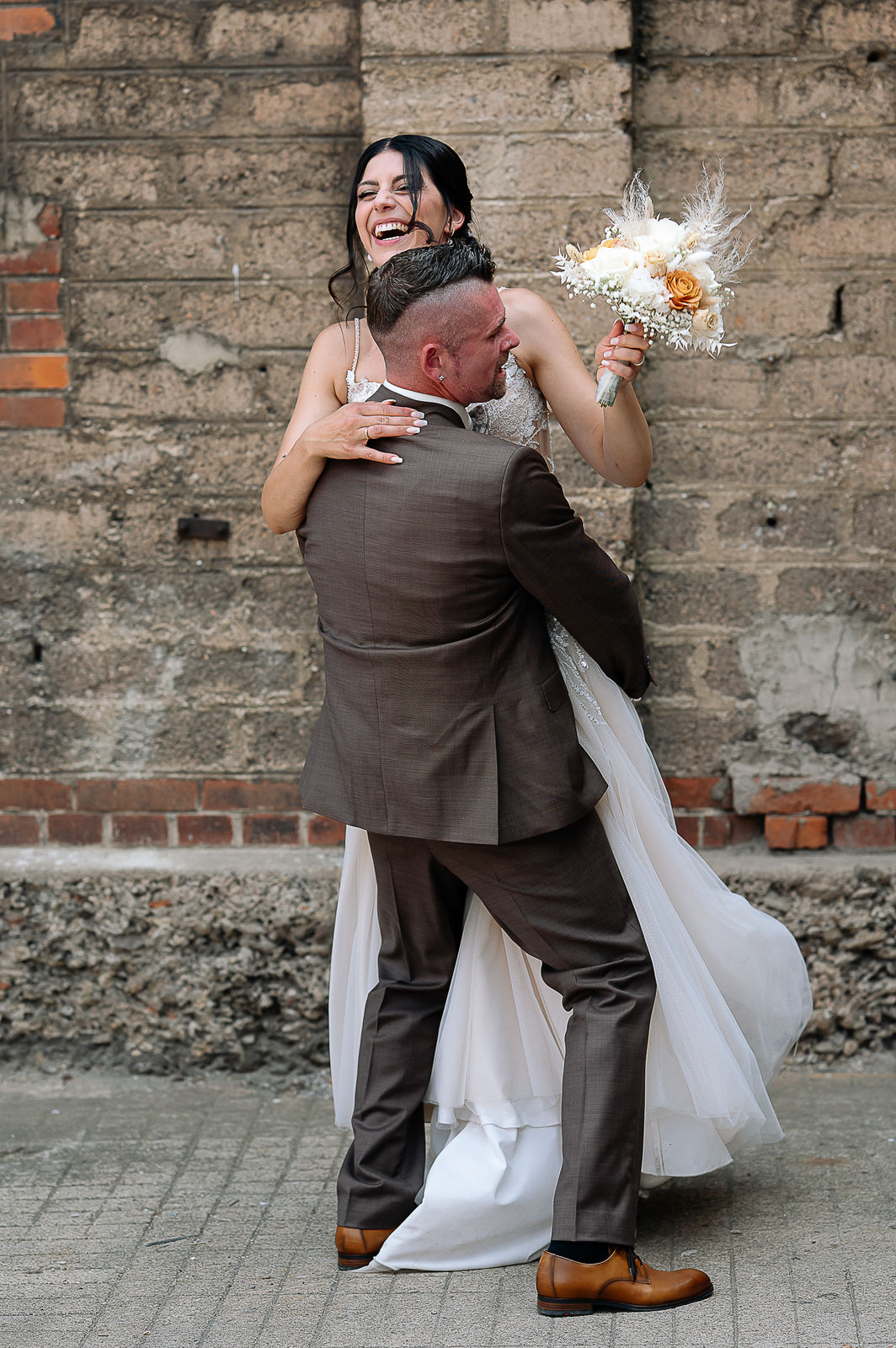 Brautpaar Sara und Olli bei ihrer Hochzeit in der Motorworld Village Metzingen vor historischer Backsteinkulisse.