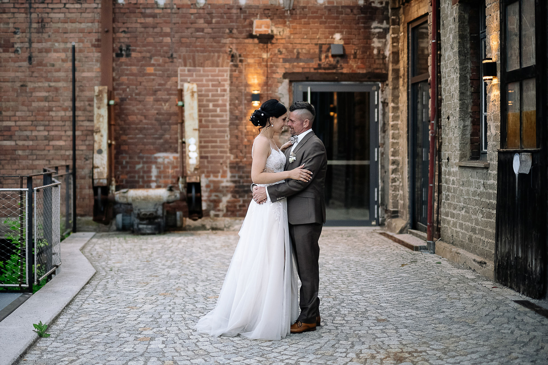 Brautpaar Sara und Olli bei ihrer Hochzeit in der Motorworld Village Metzingen vor historischer Backsteinkulisse.