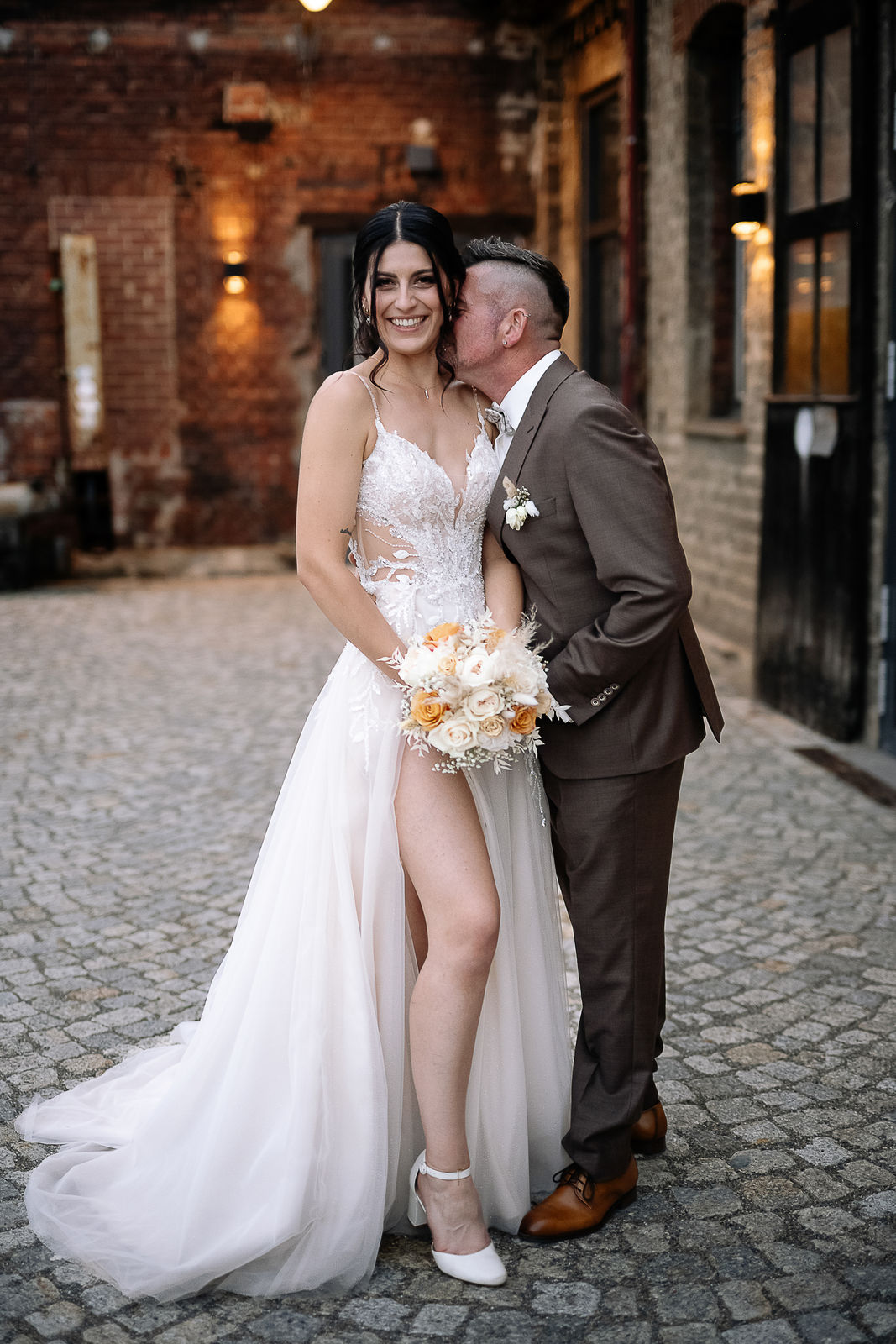 Brautpaar Sara und Olli bei ihrer Hochzeit in der Motorworld Village Metzingen vor historischer Backsteinkulisse.