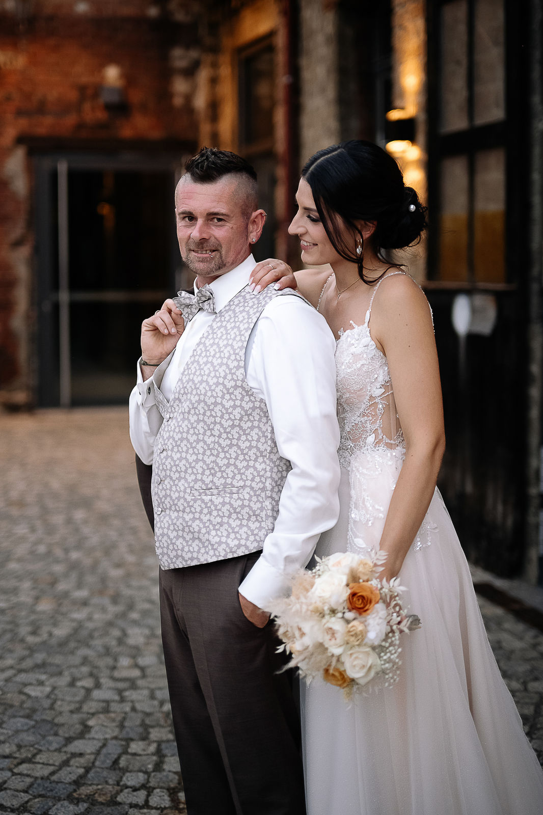 Brautpaar Sara und Olli bei ihrer Hochzeit in der Motorworld Village Metzingen vor historischer Backsteinkulisse.
