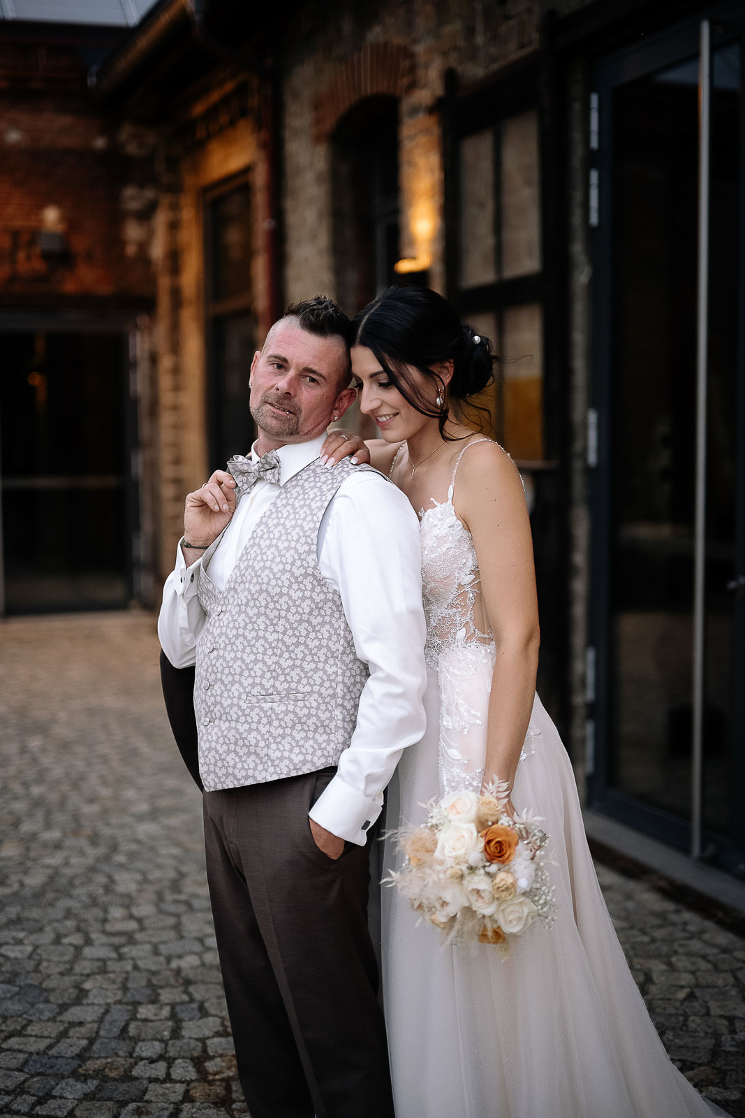 Brautpaar Sara und Olli bei ihrer Hochzeit in der Motorworld Village Metzingen vor historischer Backsteinkulisse.