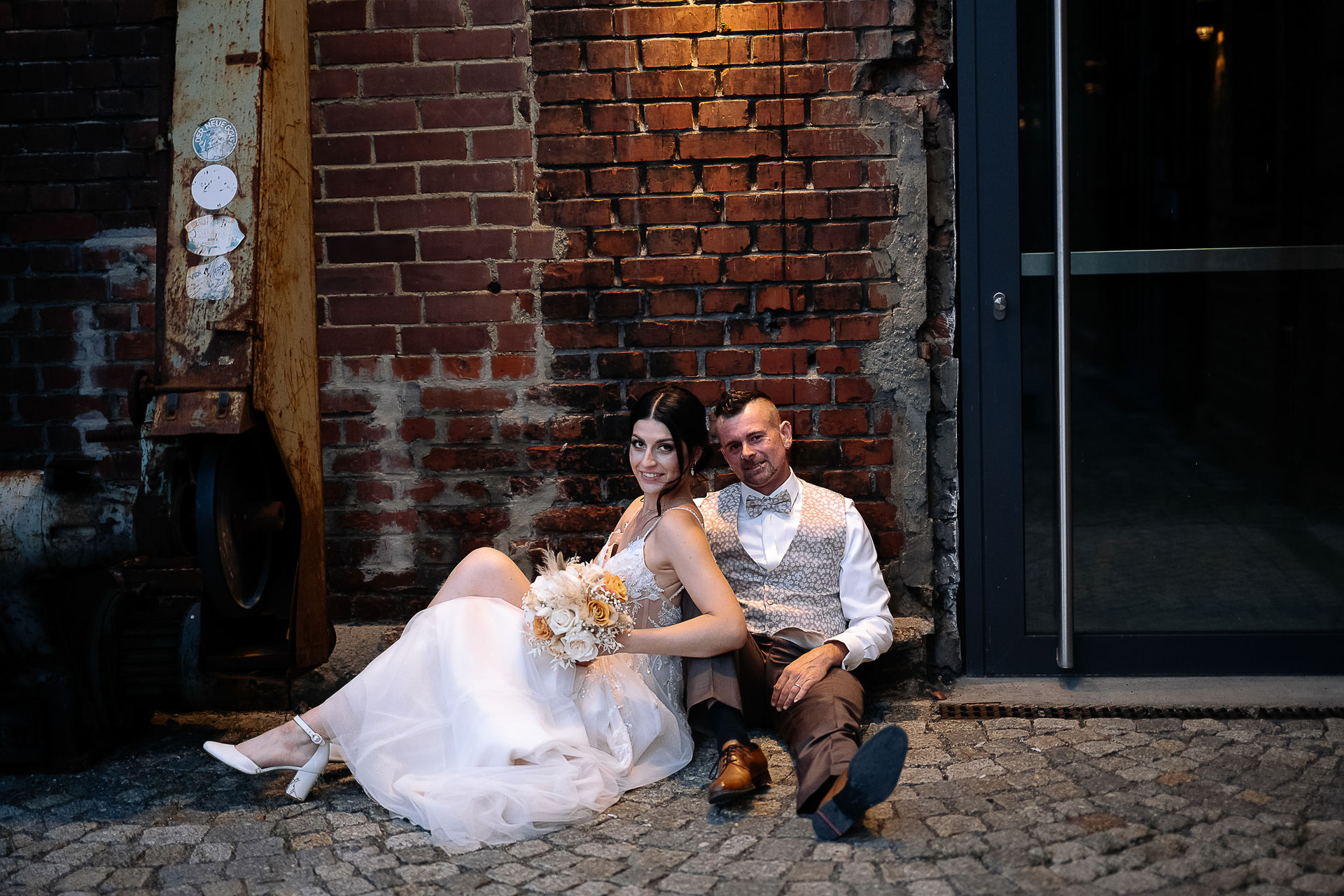 Brautpaar Sara und Olli bei ihrer Hochzeit in der Motorworld Village Metzingen vor historischer Backsteinkulisse.