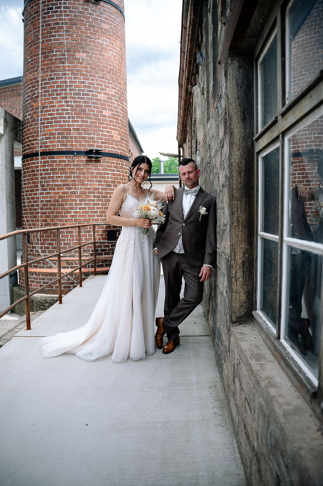 Brautpaar Sara und Olli bei ihrer Hochzeit in der Motorworld Village Metzingen vor historischer Backsteinkulisse.