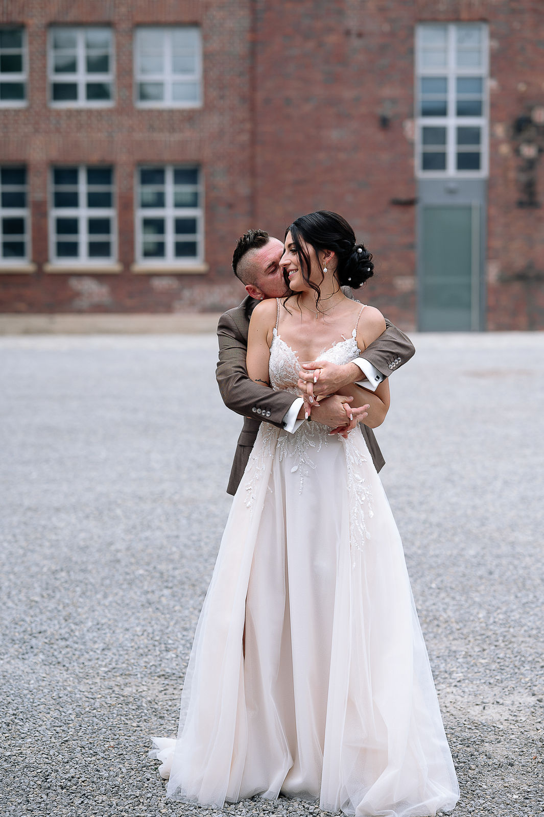 Brautpaar Sara und Olli bei ihrer Hochzeit in der Motorworld Village Metzingen vor historischer Backsteinkulisse.