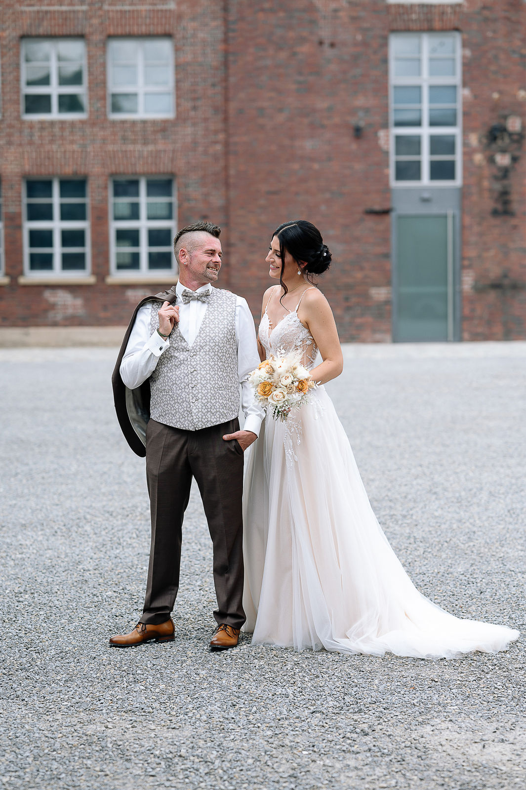 Brautpaar Sara und Olli bei ihrer Hochzeit in der Motorworld Village Metzingen vor historischer Backsteinkulisse.