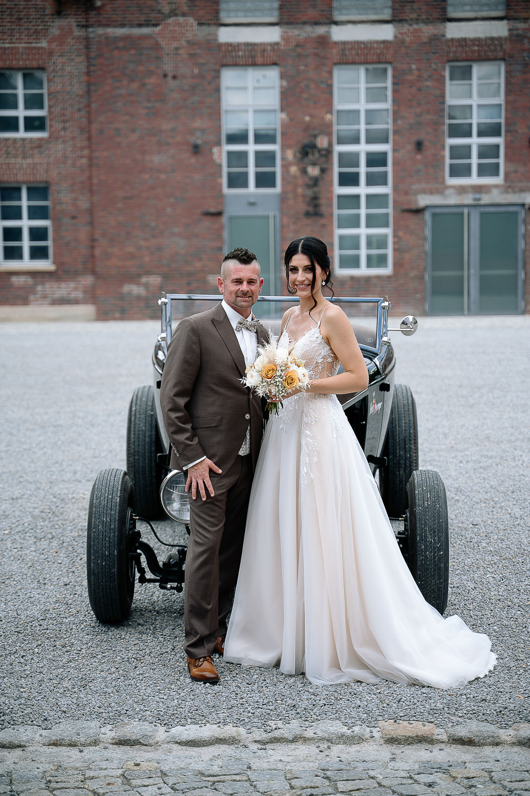 Brautpaar Sara und Olli bei ihrer Hochzeit in der Motorworld Village Metzingen vor historischer Backsteinkulisse.