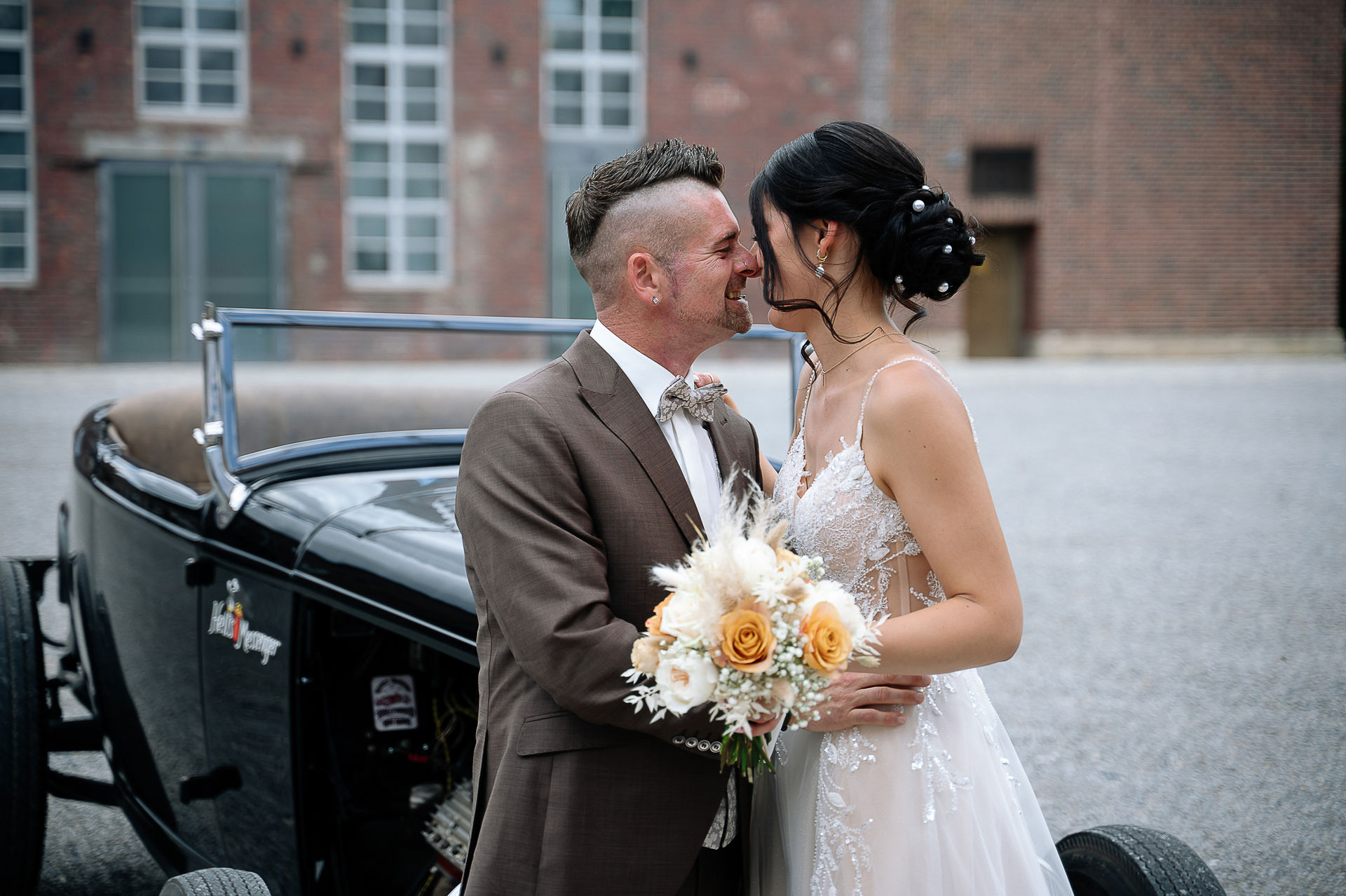 Brautpaar Sara und Olli bei ihrer Hochzeit in der Motorworld Village Metzingen vor historischer Backsteinkulisse.